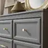 Серый деревянный комод с четырьмя ящиками, расположенный в комнате с деревянной стеной и декоративными зеркалами.