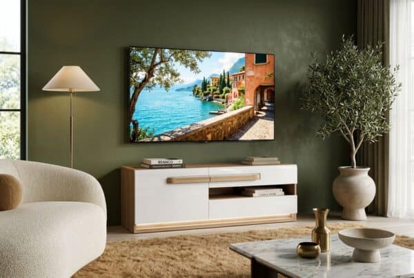 תמונה של סלון מודרני עם טלוויזיה על קיר ירוק, שידה לבנה, עציץ גדול, וכורסה קרובה, עם תאורה רכה ומרפסת עם נוף לים.
